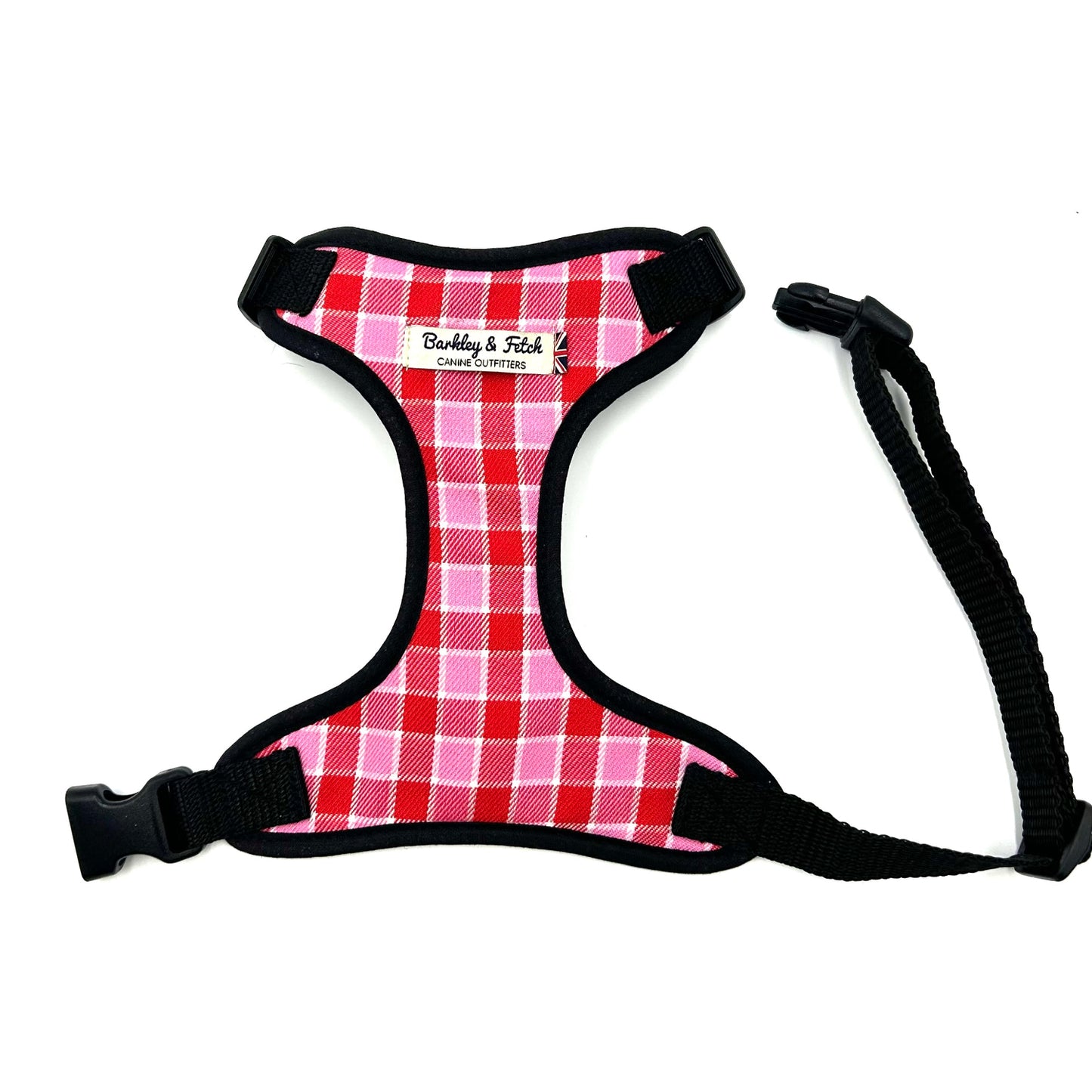 A pink and red tartan fabric harness with a black strap and buckle, designed for dogs.
