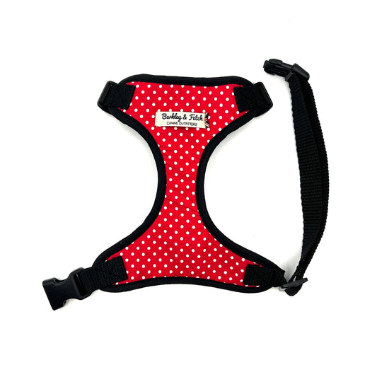 A red and white polka dot dog harness with black straps and a welded heavy duty d-ring, adjustable at neck and girth with side release buckle.