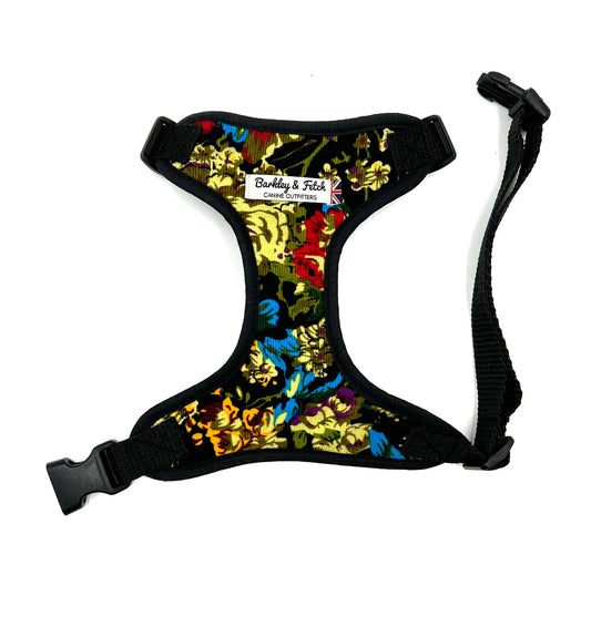 A floral patterned dog harness with adjustable straps and a metal d-ring, predominantly black with multicolored flowers.