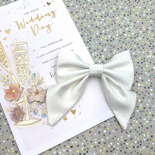 White bow on a wedding card with champagne and flowers on a heart-patterned background handmade by barkley and fetch uk
