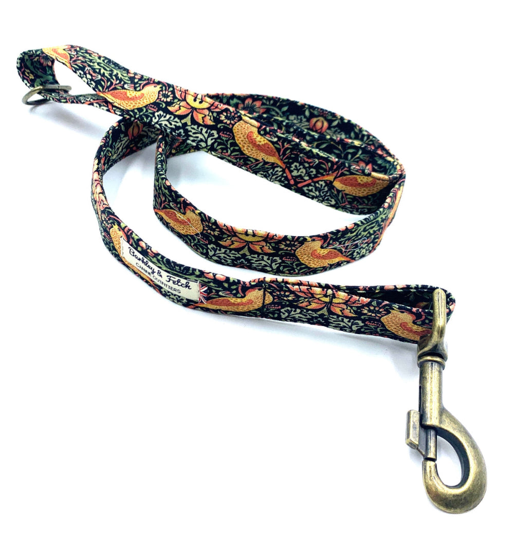 A dog lead with a floral pattern in black, green, and pink colors, featuring a metal trigger hook and a D-ring on the handle.