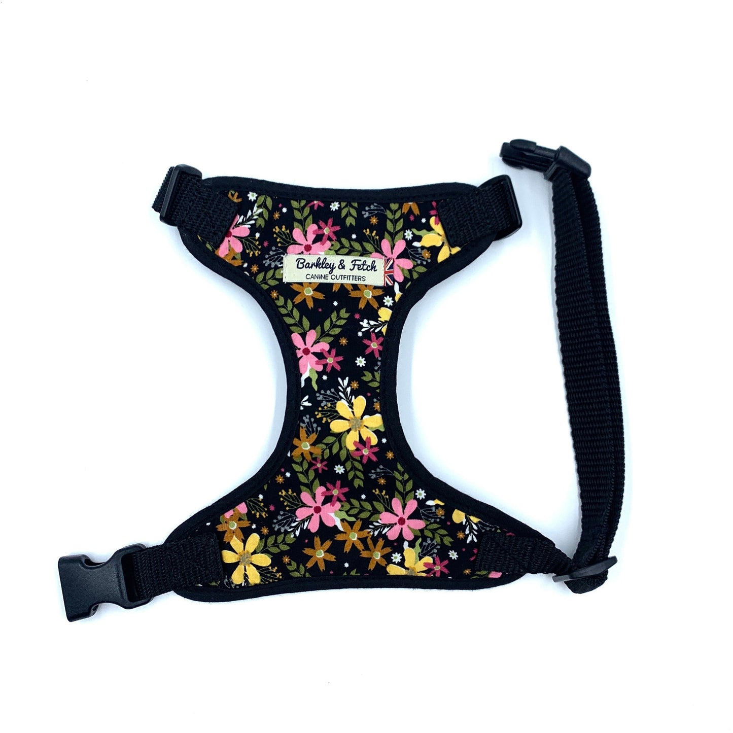 A black dog harness with a floral print design, featuring a label that says 'Barkley and Fetche'. It includes adjustable straps and a side release buckle.