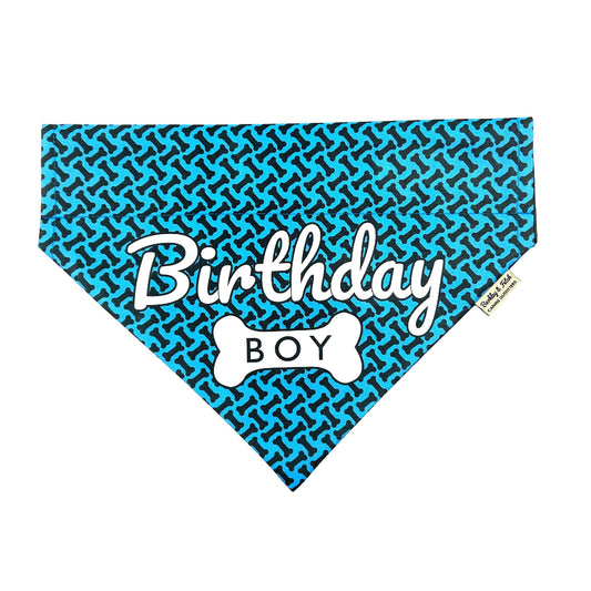 A blue dog bandana with 'Birthday BOY' printed in white, attached to a collar.