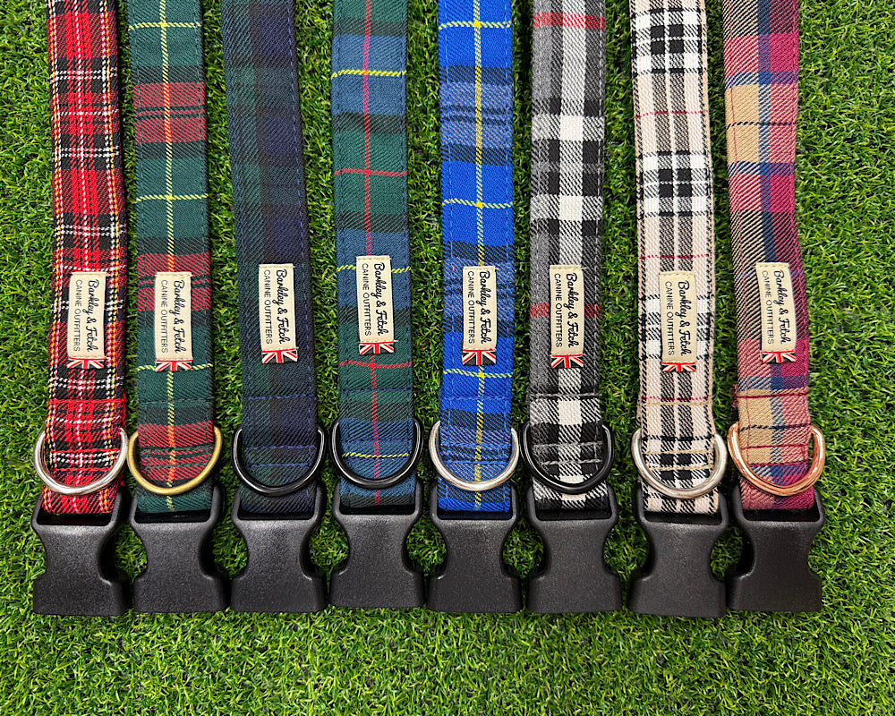Eight plaid dog collars in different tartan patterns are lined up vertically on a green artificial grass background. Each collar has a black plastic quick-release buckle and a metal ring at the bottom, with a small fabric brand tag reading Barkley and Fetch attached near the collar end.