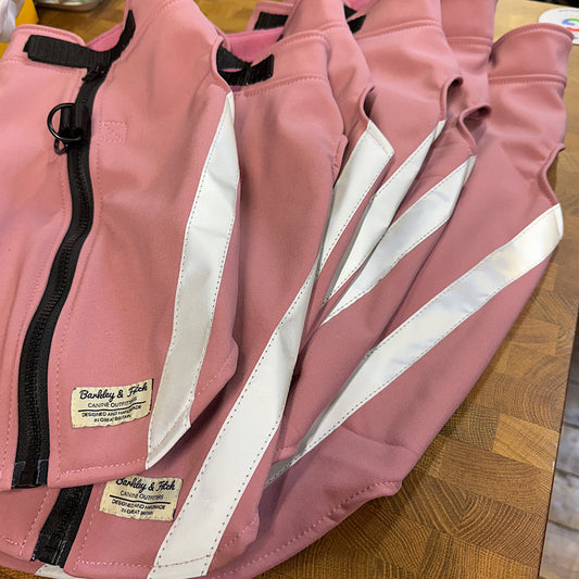 Pink jacket with reflective stripes and a brand label on a wooden surface handmade by Barkley and Fetch