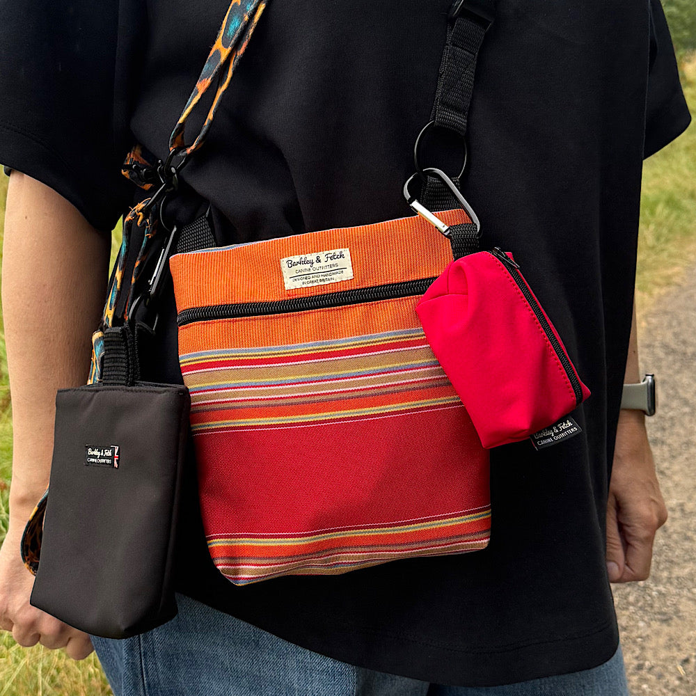 A person wearing a black T-shirt carries a small crossbody bag with a multicolor striped pattern, a bright red pouch, and a black phone case. The brand name 'Barkley and fetch' is visible on the labels.