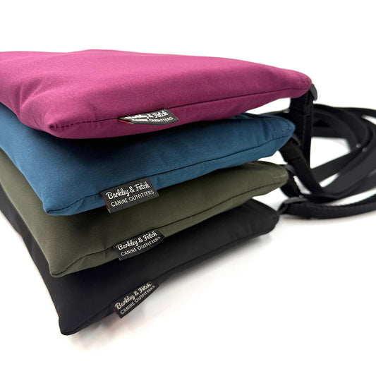 Four coloured settle mats folded into their velcro closed bags with a black shoulder straps handmade by Barkley and fetch in the UK, against a white background