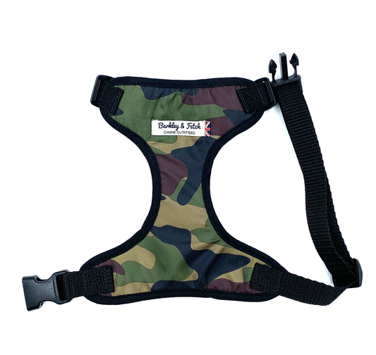 A camo print dog harness with adjustable straps and a metal d-ring, predominantly in green, brown, and black tones.