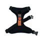 Black dog harness with orange reflective strip on a white background