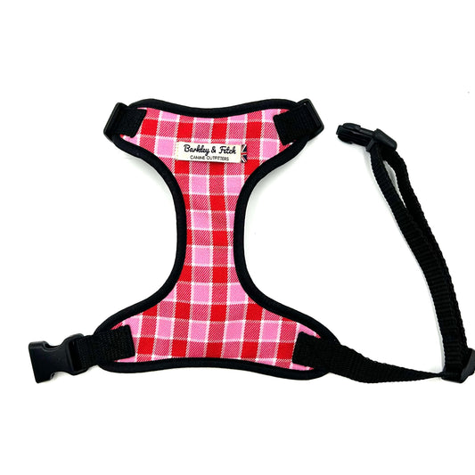 A pink and red tartan fabric harness with a black strap and buckle, designed for dogs.