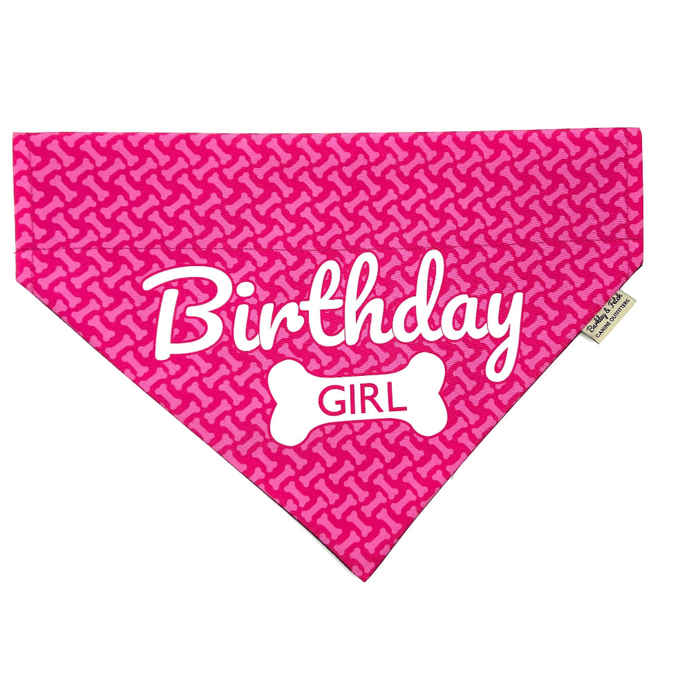 A pink dog bandana with 'Birthday Girl' text and a bone pattern design, intended to slide onto a dog's collar.