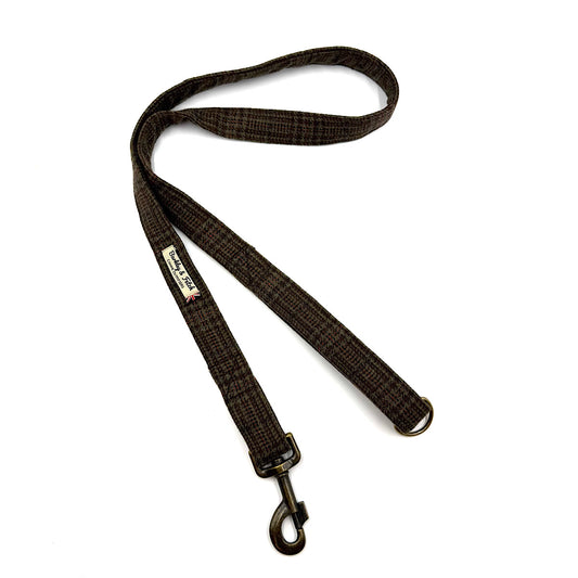 A dark brown and black plaid dog leash with a brass-coloured swivel snap hook and a small brand label, shown on a plain white background. Handmade in Great Britain by Barkley and Fetch.