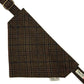 A triangular dog bandana with a brown, black, and red plaid pattern, featuring a matching strap with a brass buckle and a brand label Handmade in Great Britain by Barkley and Fetch.