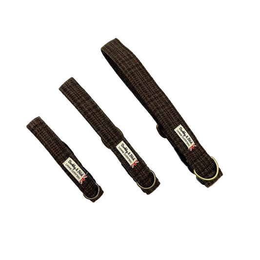 Three dark brown woven fabric dog collars of different sizes arranged diagonally on a white background, each with a brass ring and a brand label. Handmade in Great Britain by Barkley and Fetch.