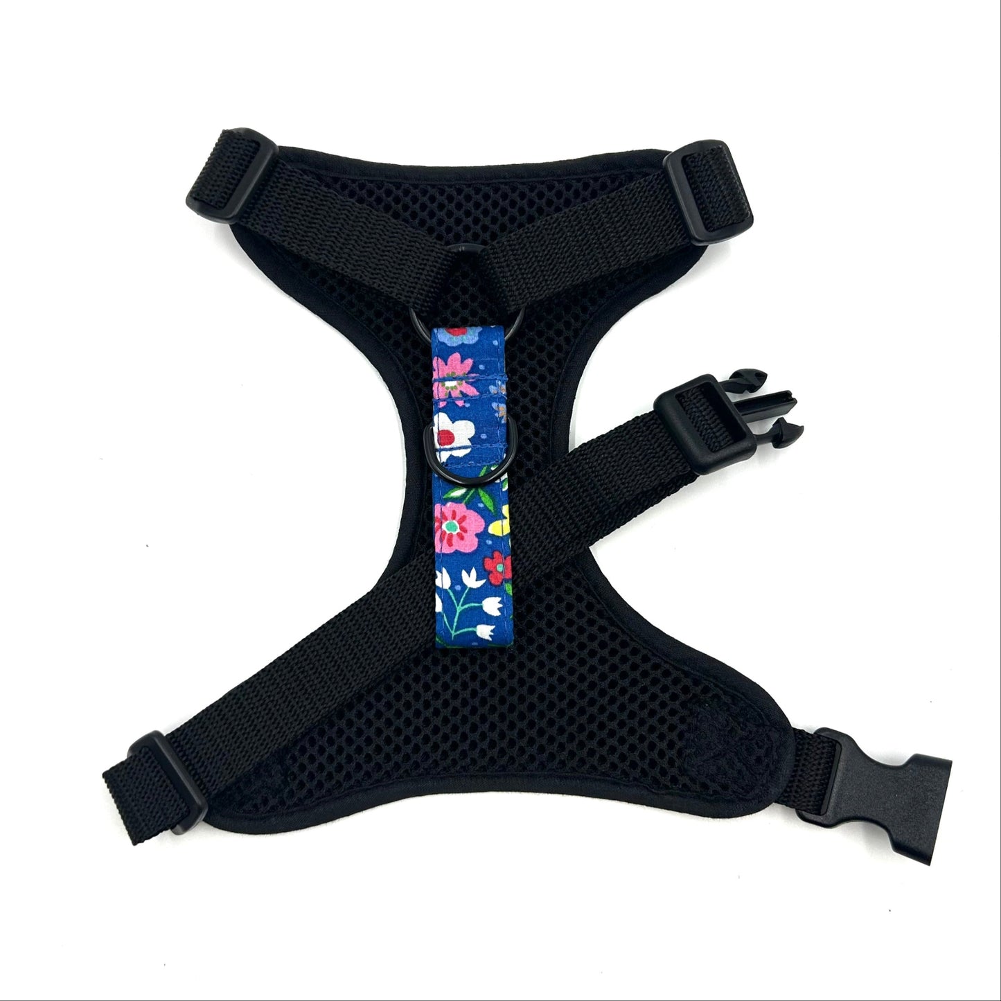 Black dog harness with a colorful floral patch on a white background