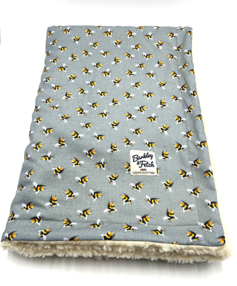 A grey dog blanket with a pattern of bees and the brand label 'Barkley & Fetch' visible.