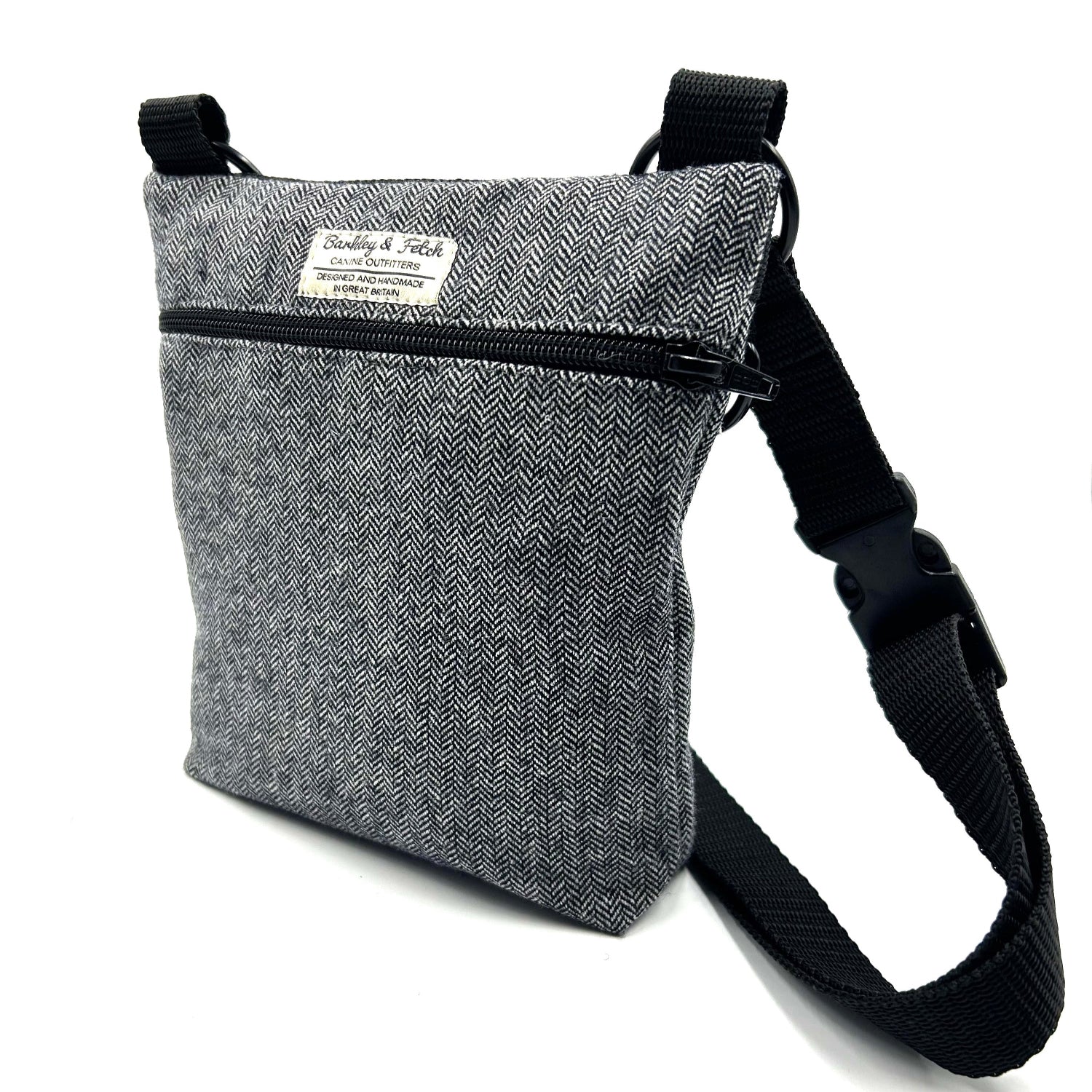 A gray herringbone patterned dog walk and treat bag with an adjustable black shoulder strap and a zip fastening.