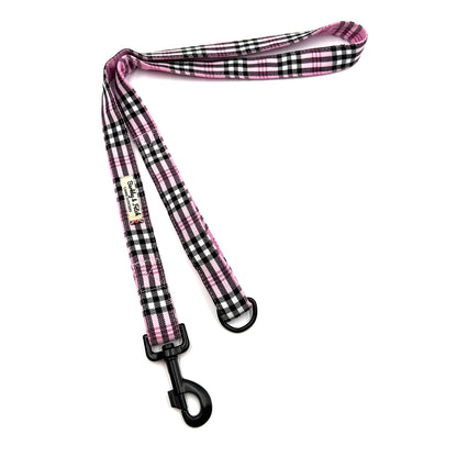 Pink and black plaid dog leash with a clip on a white background