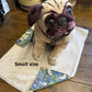 Stuffed pug dog toy on a fabric blanket with a basket in the background