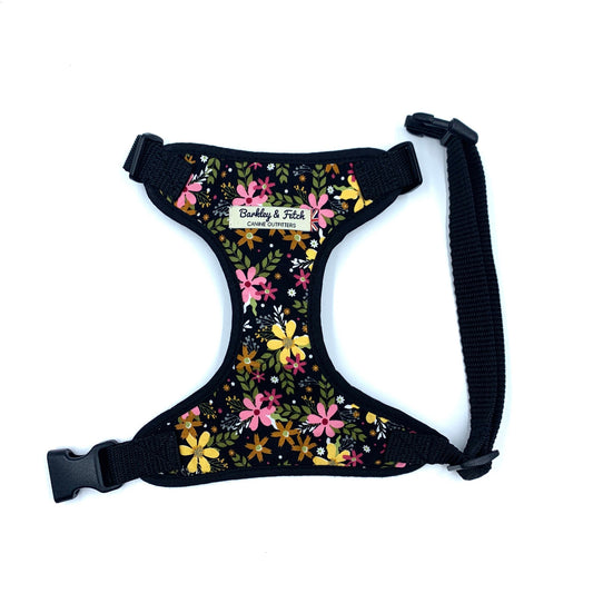 A black dog harness with a floral print design, featuring a label that says 'Barkley and Fetche'. It includes adjustable straps and a side release buckle.