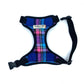 A checkered pink and blue fabric dog harness with a black side release buckle and webbing, and a branded label at the neck.