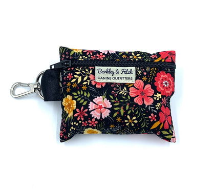 A floral print poo bag holder with a label that reads 'Barkly & Fetch'. It has a keyring attachment and is primarily black with colorful flower patterns.