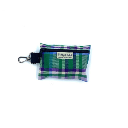 A green and purple check patterned poo bag holder with a black clip and a brand tag displayed at the top.