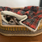 Dog lying in a wicker pet bed with a plaid blanket