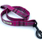 A pink and grey tartan pattern dog lead with a metal trigger hook and a D-ring on the handle.