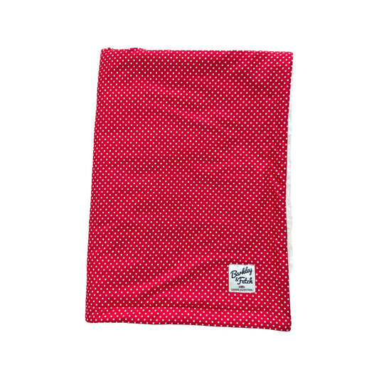 A red dog blanket with a white polka dot pattern and a brand tag showing on the lower corner handmade in the UK by Barkley And Fetch